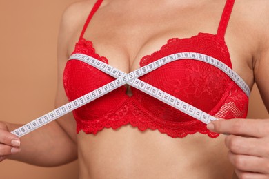 Photo of Woman in beautiful bra measuring breast circumference on beige background, closeup