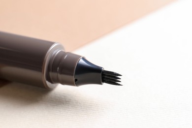Photo of Brown liquid eyebrow pencil on beige background, closeup. Space for text