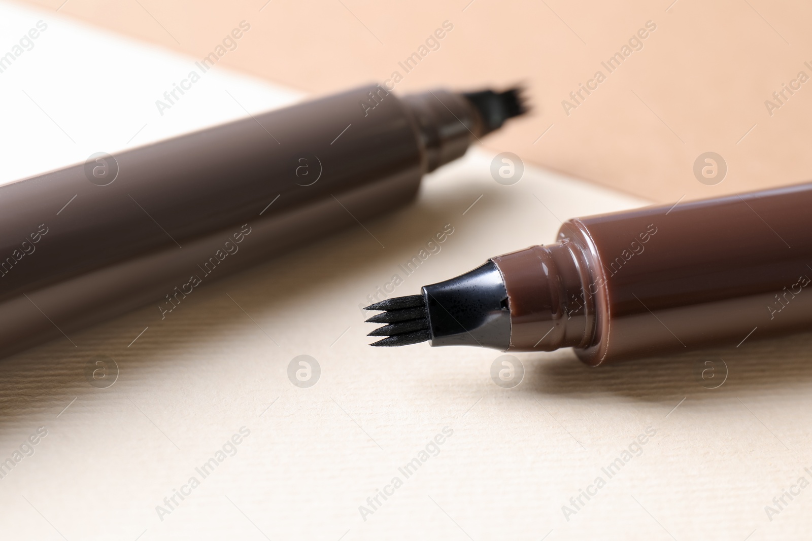 Brown liquid eyebrow pencils on beige background, closeup Photo of Brown liquid eyebrow pencils on beige background, closeup