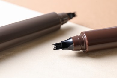 Photo of Brown liquid eyebrow pencils on beige background, closeup