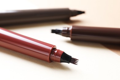 Photo of Different liquid eyebrow pencils on beige background, closeup