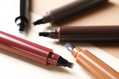 Photo of Different liquid eyebrow pencils on beige background, closeup