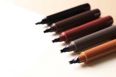 Photo of Different liquid eyebrow pencils on beige background, closeup. Space for text