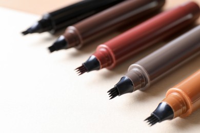 Photo of Different liquid eyebrow pencils on beige background, closeup. Space for text