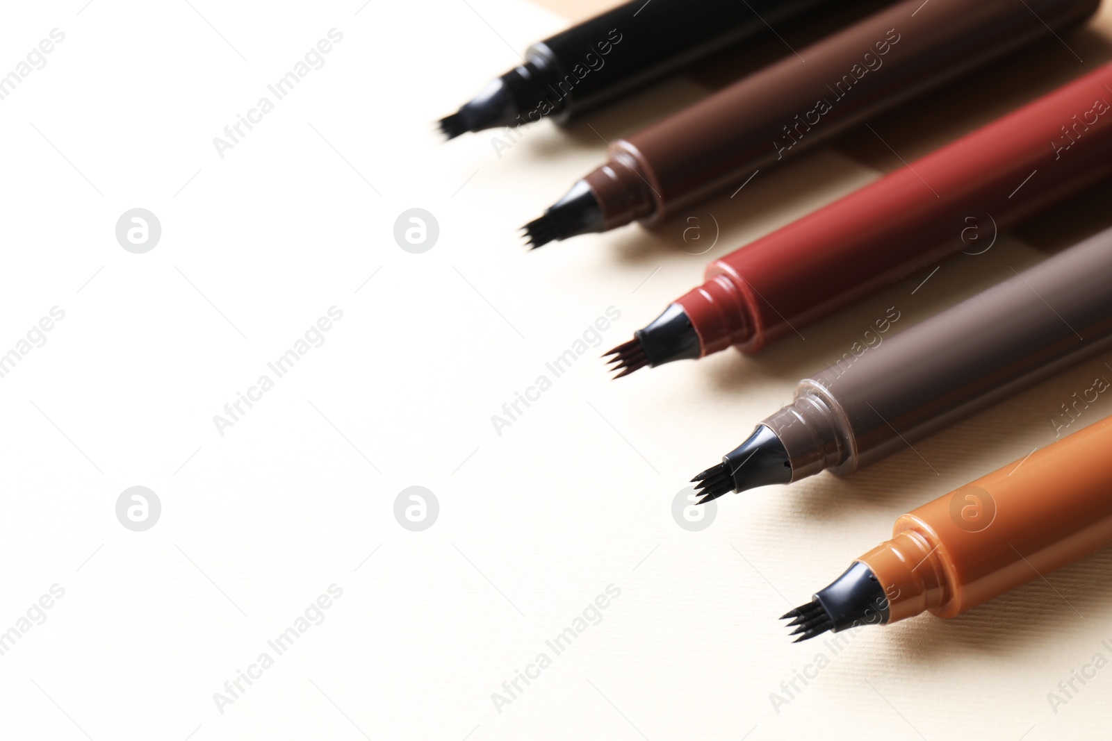 Different liquid eyebrow pencils on beige background, closeup. Space for text Photo of Different liquid eyebrow pencils on beige background, closeup. Space for text