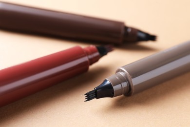 Photo of Different liquid eyebrow pencils on beige background, closeup