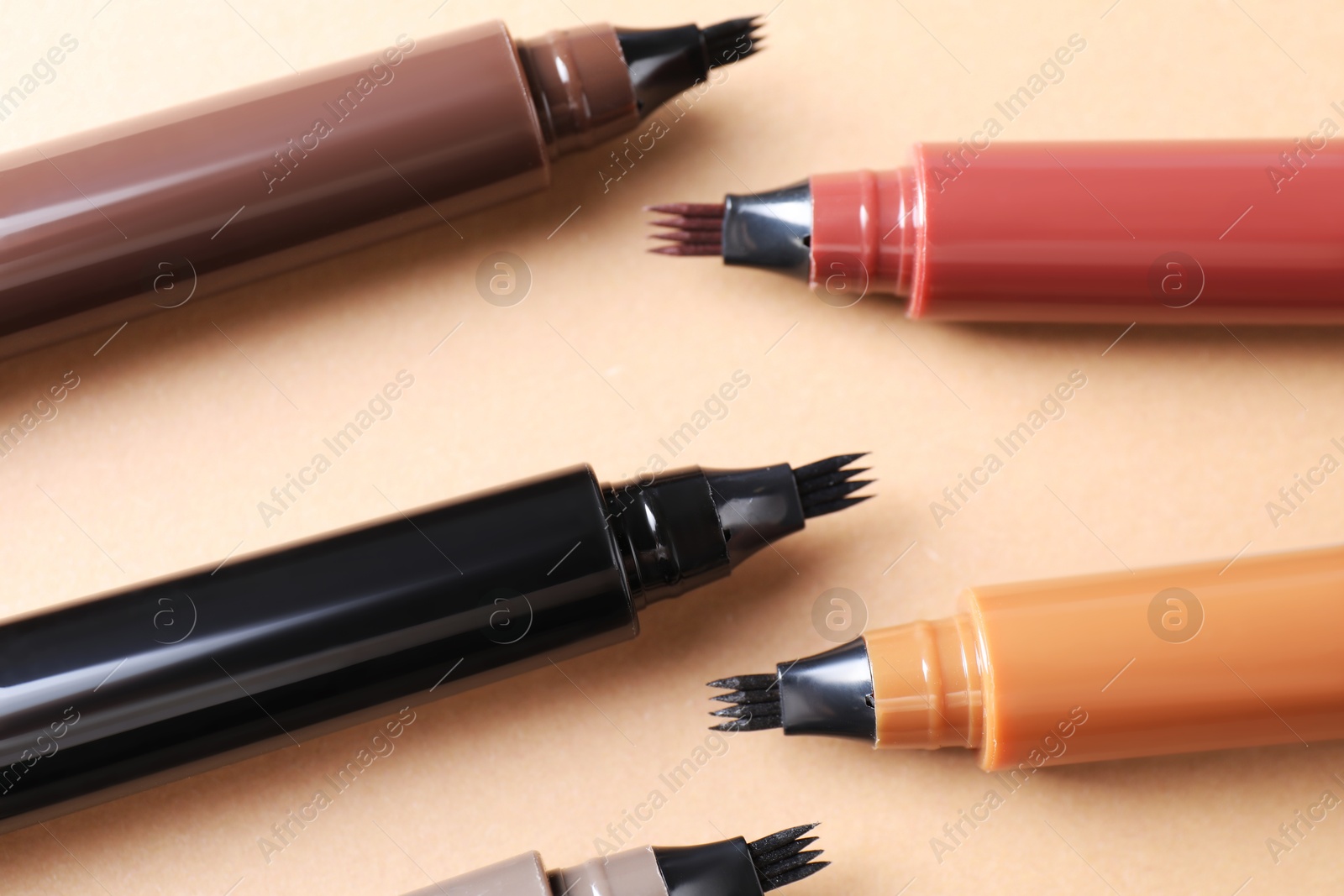 Different liquid eyebrow pencils on beige background, flat lay Photo of Different liquid eyebrow pencils on beige background, flat lay