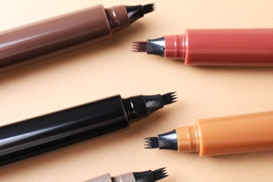 Photo of Different liquid eyebrow pencils on beige background, flat lay
