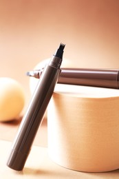 Photo of Stylish presentation of liquid eyebrow pencils on beige background, closeup