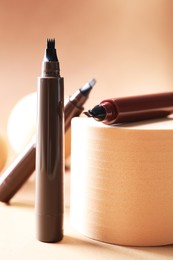 Photo of Stylish presentation of liquid eyebrow pencils on beige background, closeup