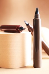 Photo of Stylish presentation of liquid eyebrow pencils on beige background, closeup