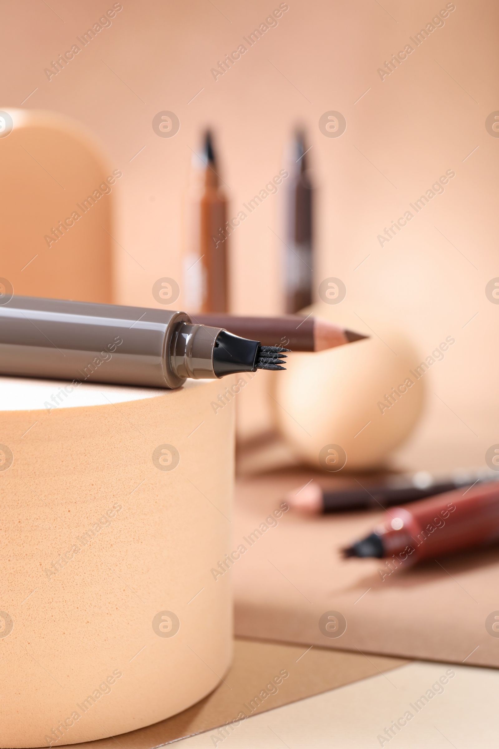 Stylish presentation of liquid eyebrow pencils on beige background, closeup Photo of Stylish presentation of liquid eyebrow pencils on beige background, closeup