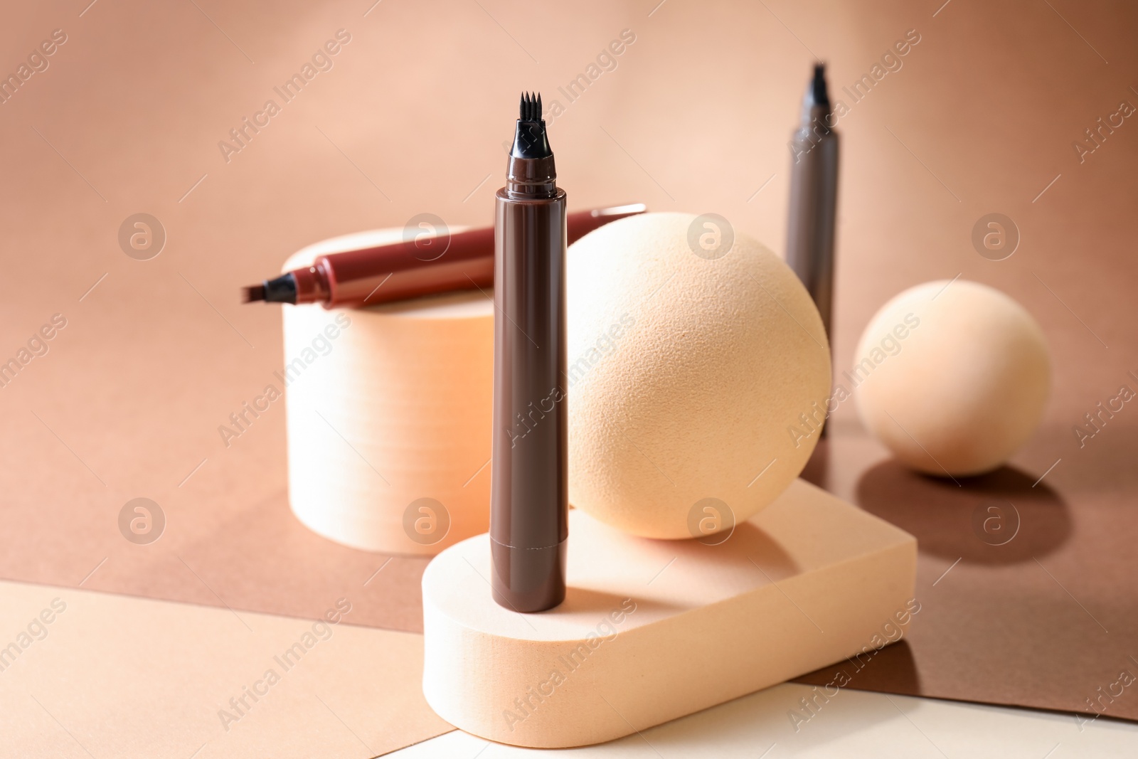 Stylish presentation of liquid eyebrow pencils on beige background, closeup Photo of Stylish presentation of liquid eyebrow pencils on beige background, closeup