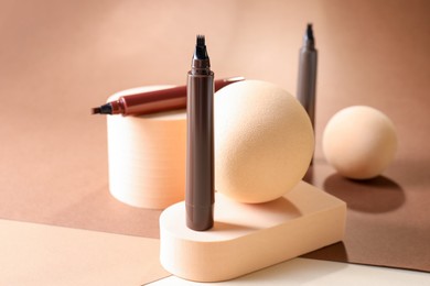 Photo of Stylish presentation of liquid eyebrow pencils on beige background, closeup