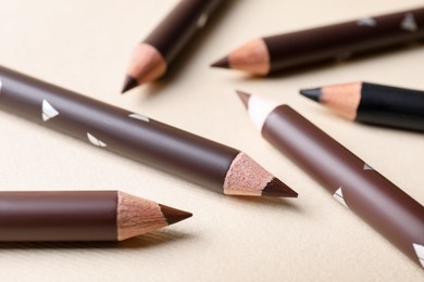 Photo of Different eyebrow pencils on beige background, closeup