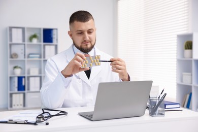 Photo of Doctor with pills having online consultation via laptop in clinic