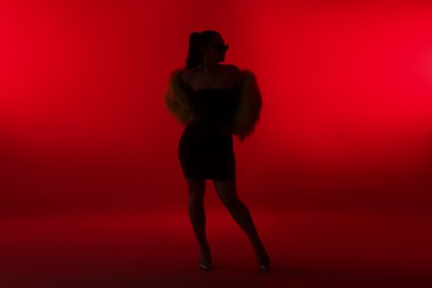 Photo of Silhouette of woman in stylish outfit posing on red background