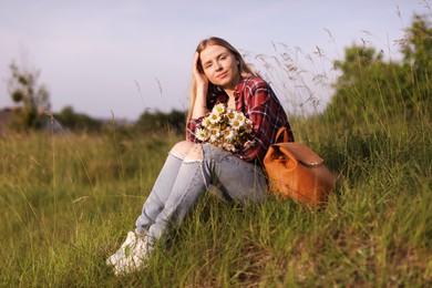Photo of Beautiful woman with wildflowers and backpack enjoying summer day in meadow