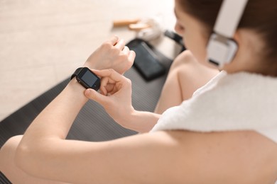 Photo of Woman checking fitness tracker during training indoors, closeup