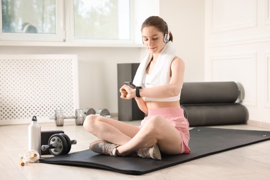 Photo of Woman checking fitness tracker during training indoors
