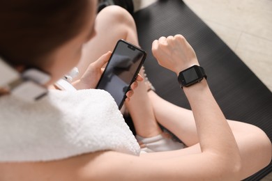 Photo of Woman checking fitness tracker during training indoors, closeup