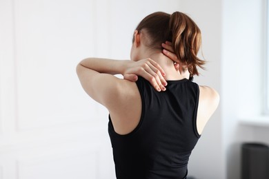 Photo of Sports injury. Young woman suffering from shoulder pain in fitness studio, back view