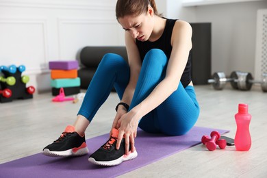 Photo of Sports injury. Young woman suffering from leg pain in fitness studio