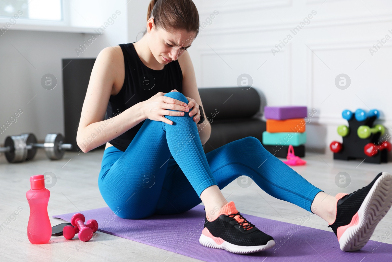 Sports injury. Young woman suffering from knee pain in fitness studio Photo of Sports injury. Young woman suffering from knee pain in fitness studio