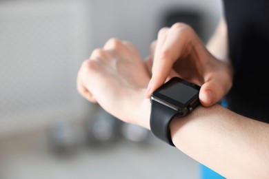 Photo of Woman checking fitness tracker during training indoors, closeup