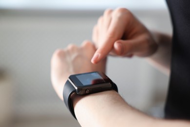 Photo of Woman checking fitness tracker during training indoors, closeup