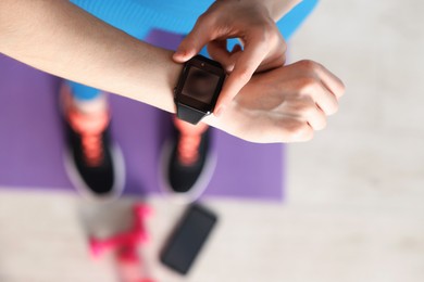 Photo of Woman checking fitness tracker during training indoors, above view