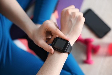 Photo of Woman checking fitness tracker during training indoors, closeup