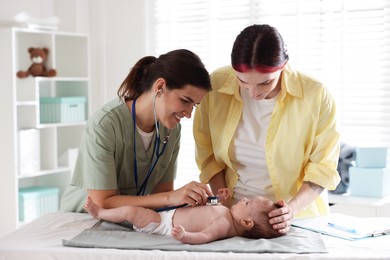 Photo of Mother and her cute little child having appointment with pediatrician in hospital. Doctor examining baby with stethoscope