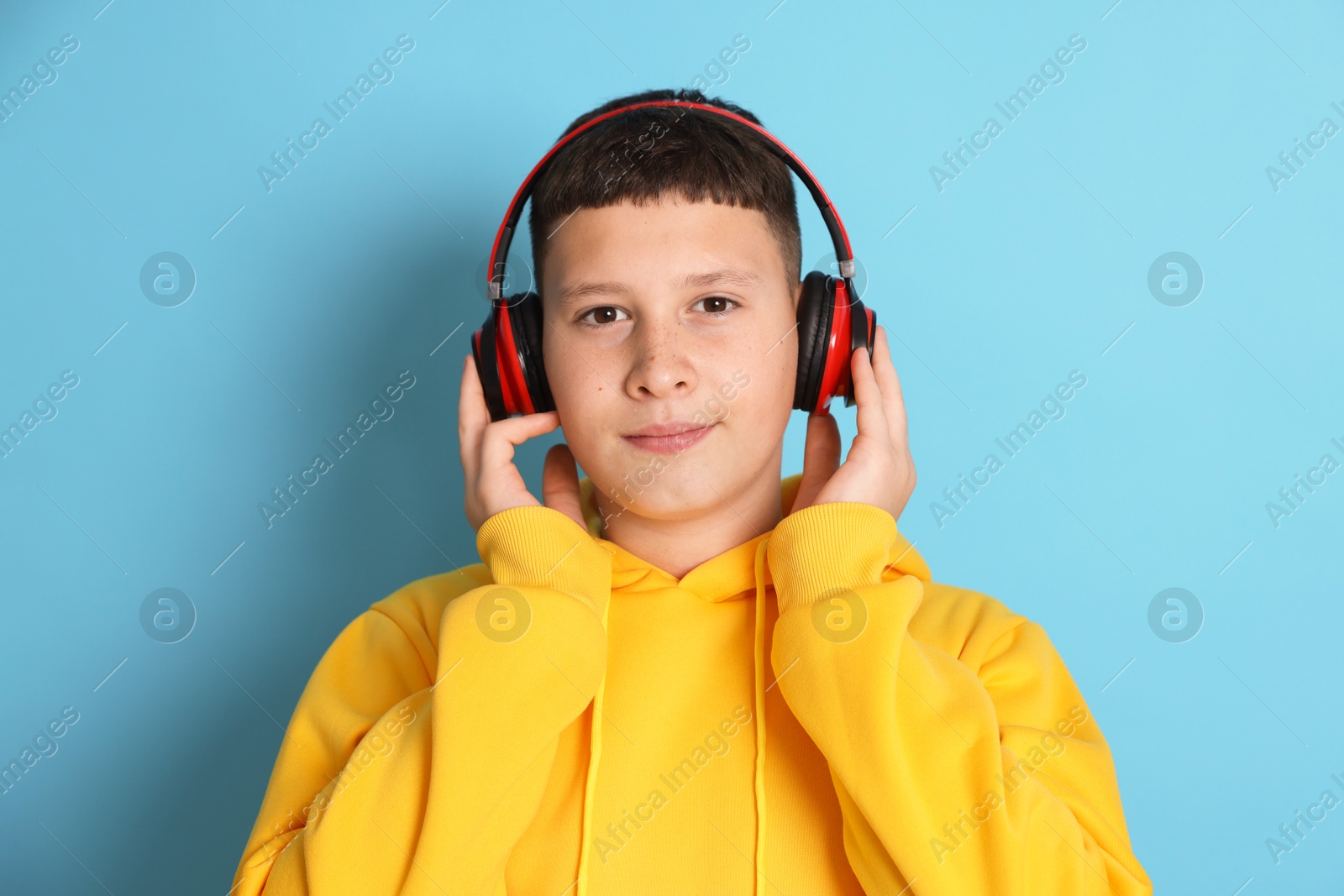 Teenage boy in headphones on light blue background Photo of Teenage boy in headphones on light blue background