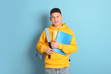 Photo of Teenage boy with backpack and notebooks on light blue background