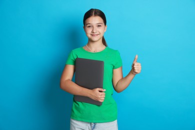 Photo of Teenage girl with laptop showing thumbs up on light blue background