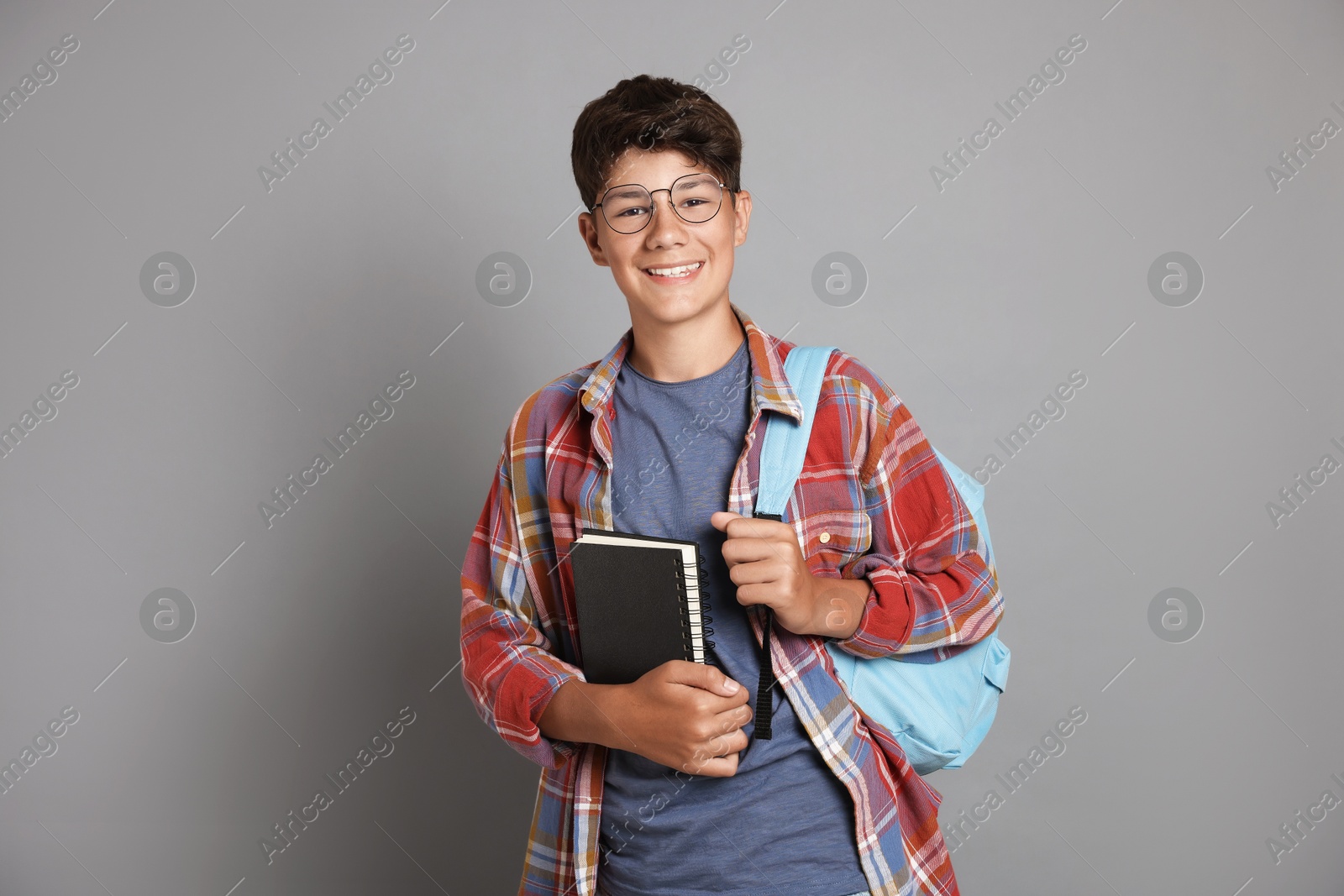 Photo of Teenage boy with notebook and backpack on grey background