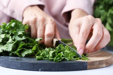 Photo of Woman cutting fresh green cilantro at light table, closeup