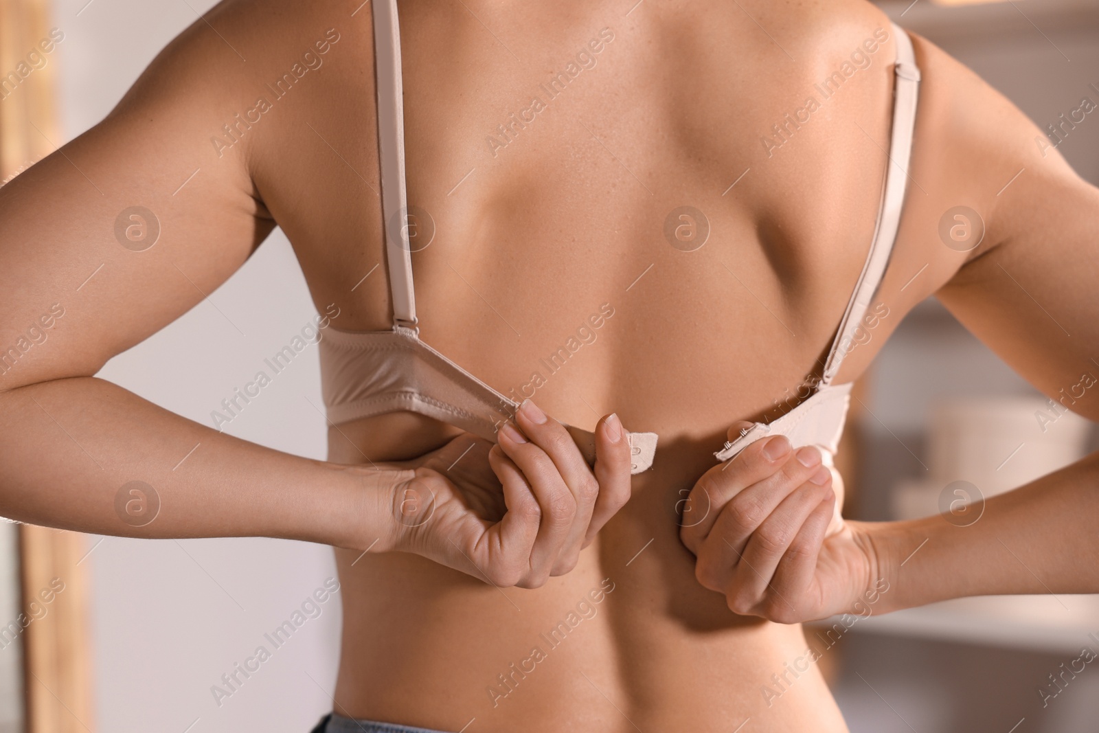 Woman putting on beige bra indoors, closeup Photo of Woman putting on beige bra indoors, closeup
