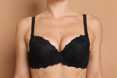 Photo of Woman wearing beautiful black bra on beige background, closeup