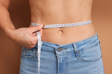 Photo of Woman measuring waist circumference on beige background, closeup