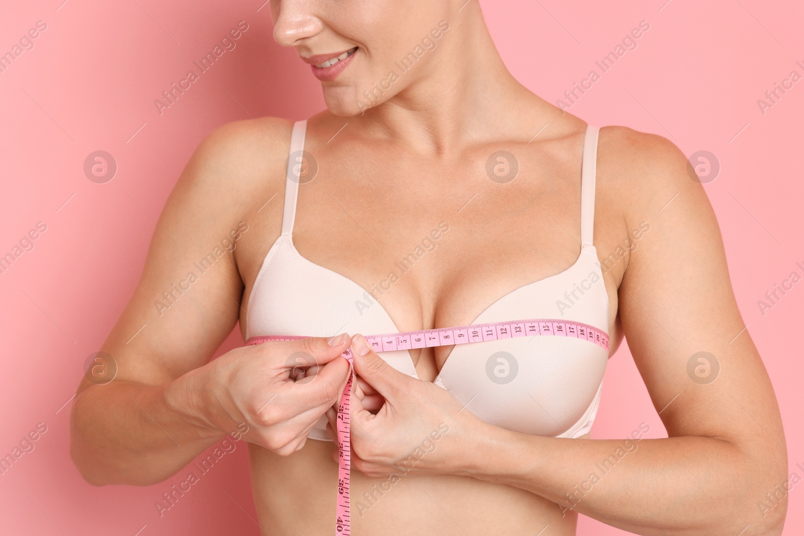 Woman in beautiful bra measuring breast circumference on pink background, closeup Photo of Woman in beautiful bra measuring breast circumference on pink background, closeup