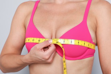 Photo of Woman in beautiful bra measuring breast circumference on light grey background, closeup