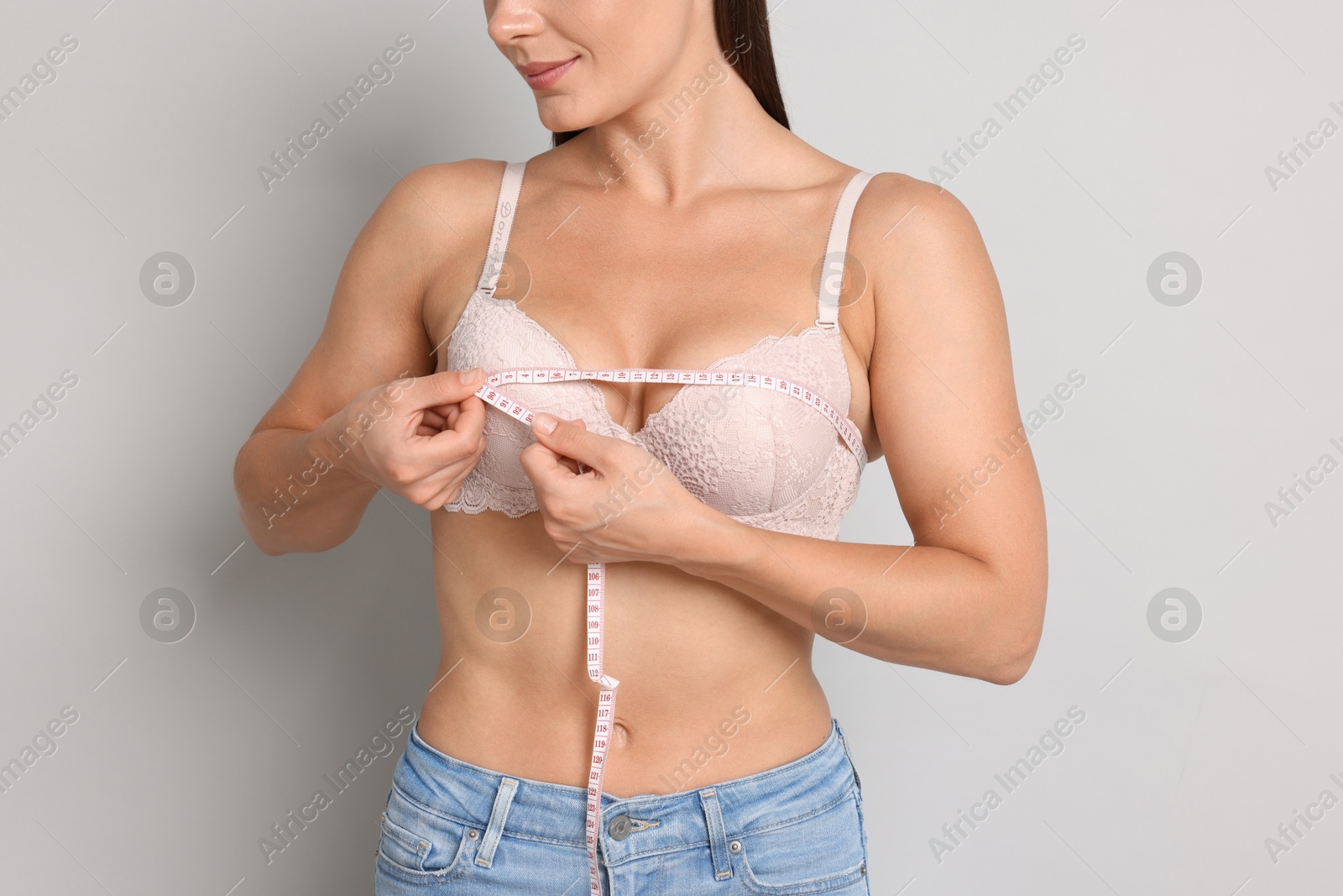 Photo of Woman in beautiful bra measuring breast circumference on light grey background, closeup