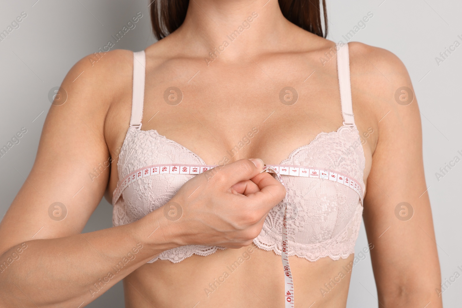 Woman in beautiful bra measuring breast circumference on light grey background, closeup Photo of Woman in beautiful bra measuring breast circumference on light grey background, closeup