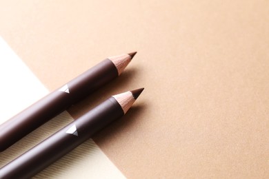 Photo of Different eyebrow pencils on beige background, closeup. Space for text