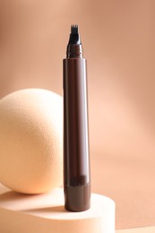 Photo of Stylish presentation of liquid eyebrow pencil on beige background, closeup