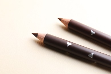 Photo of Different eyebrow pencils on beige background, closeup
