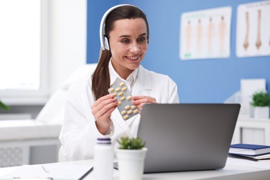 Photo of Doctor in headphones with pills having online consultation via laptop indoors