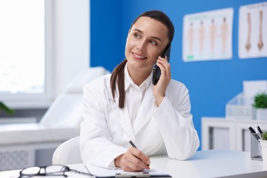 Photo of Doctor with smartphone having online consultation at table in clinic